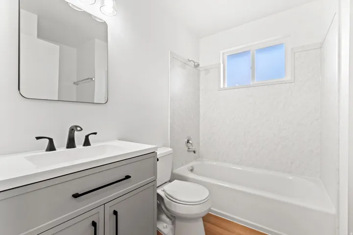 Contemporary bathroom featuring a light gray vanity with black hardware, a white integrated sink, and a black-framed mirror