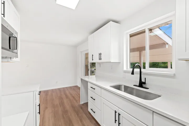Bright kitchen space featuring white cabinetry with matte black hardware, white countertops, stainless steel sink, and wood-finish flooring