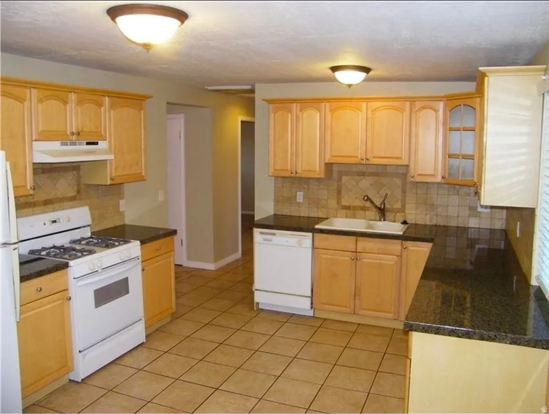 Kitchen featuring light wood cabinetry, dark countertops, tiled flooring, and a tiled backsplash