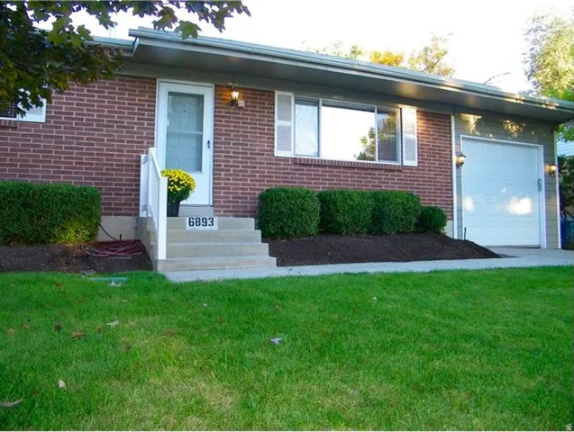 Brick exterior facade with white front door, concrete porch steps with white railings, integrated garage with white door, and landscaped shrubbery