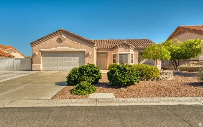 Stucco exterior with a terracotta tile roof, featuring a two-car garage, a bay window, and a gravel front yard with mature landscaping
