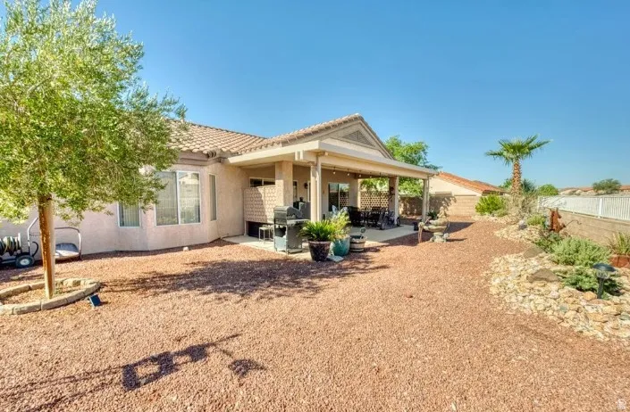 Expansive backyard featuring a covered patio, rock landscaping, mature desert plantings, and a tiled roofline