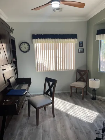 Spacious room featuring wood-finish flooring, a ceiling fan with integrated lighting, and multiple windows with vertical blinds