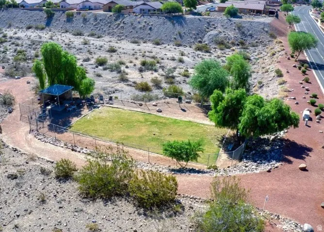 Fenced recreational area featuring a green turf lawn, shaded seating, surrounding desert landscaping, and a curvilinear pathway