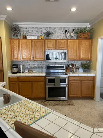 Kitchen featuring oak cabinetry, tile countertops, a stainless steel double oven range, a built-in microwave, and tile flooring