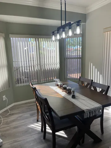 Dining area featuring light wood-finish flooring, a modern linear chandelier with five clear glass shades, a bay window with vertical blinds, and crown molding