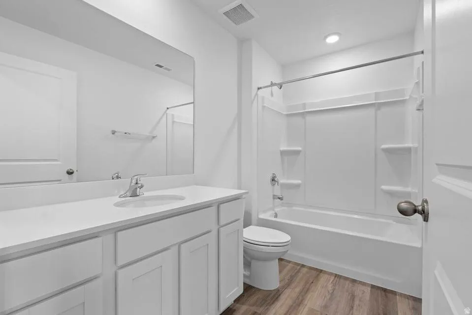 Bathroom featuring a white vanity with an integrated sink, polished chrome faucet, rectangular mirror, wood-finish flooring, and a white tub/shower combination