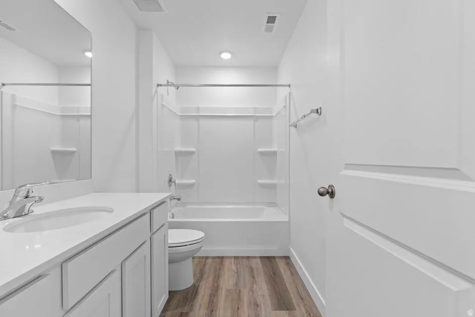 Bathroom featuring a white vanity with an integrated sink, chrome faucet, wall-mounted mirror, and wood-finish flooring