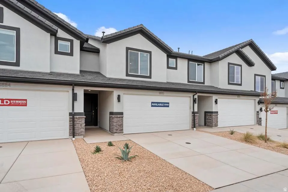 Contemporary townhome exterior featuring light gray stucco siding with dark trim accents, a dark shingle roof, and a stone veneer base