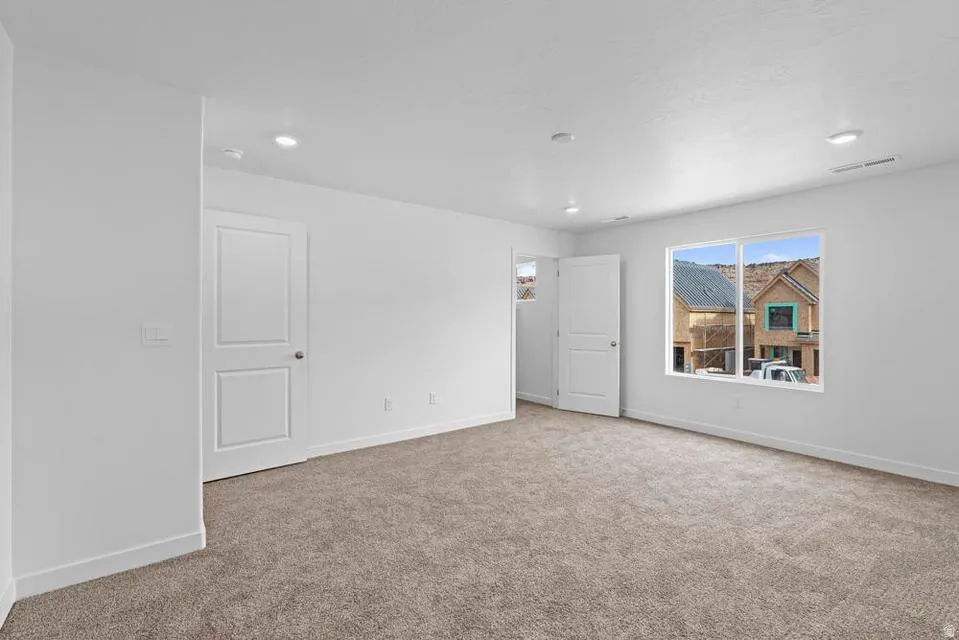 Spacious room featuring neutral carpet flooring, recessed lighting, white walls, and a large window