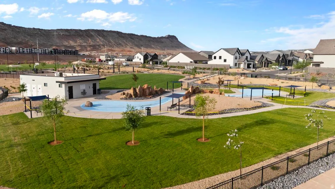 Community park featuring extensive green spaces, a splash pad, a dedicated facility building, paved walking paths, and shaded seating areas