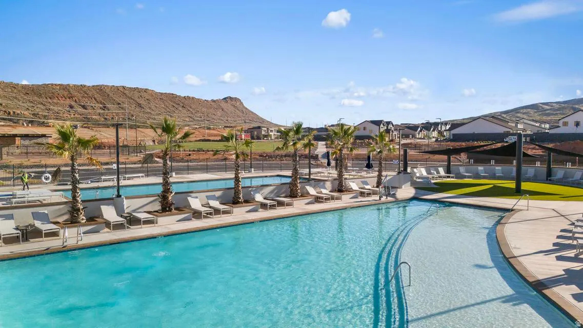 Expansive pool area featuring a curved leisure pool, multiple lounge chairs, artificial turf sections, and mature palm trees