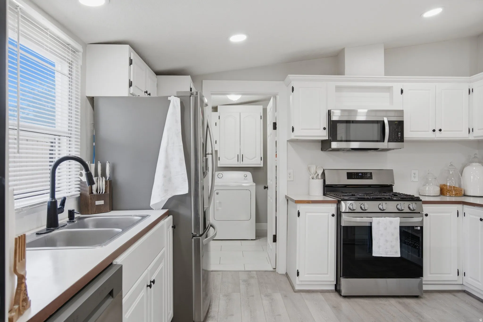 Kitchen featuring white cabinetry, stainless steel appliances, wood-finish countertops, a double basin sink with a matte black faucet, and wood-finish flooring