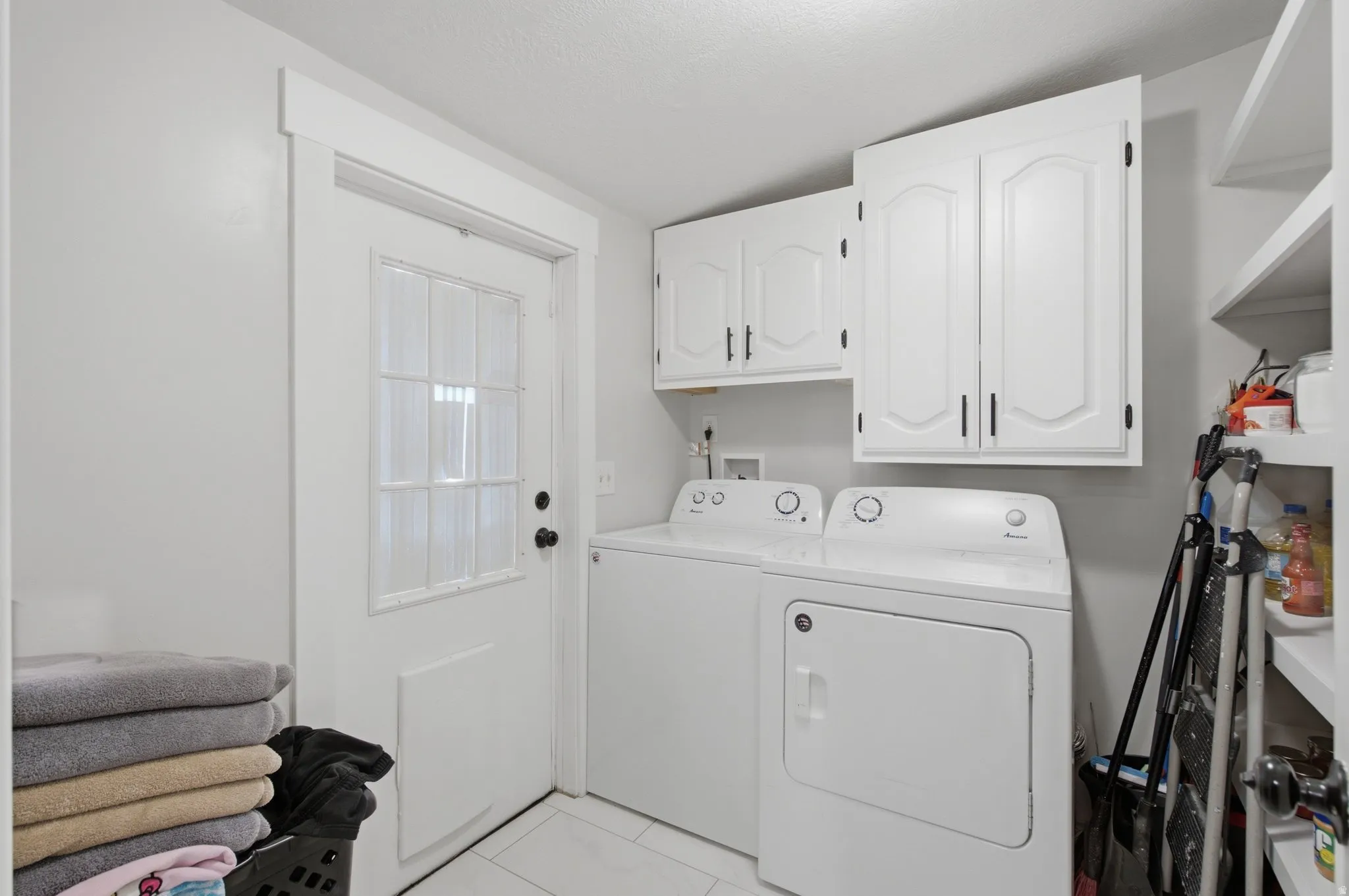 Dedicated laundry space featuring a windowed door, white cabinetry with dark hardware, built-in shelving, and tile flooring