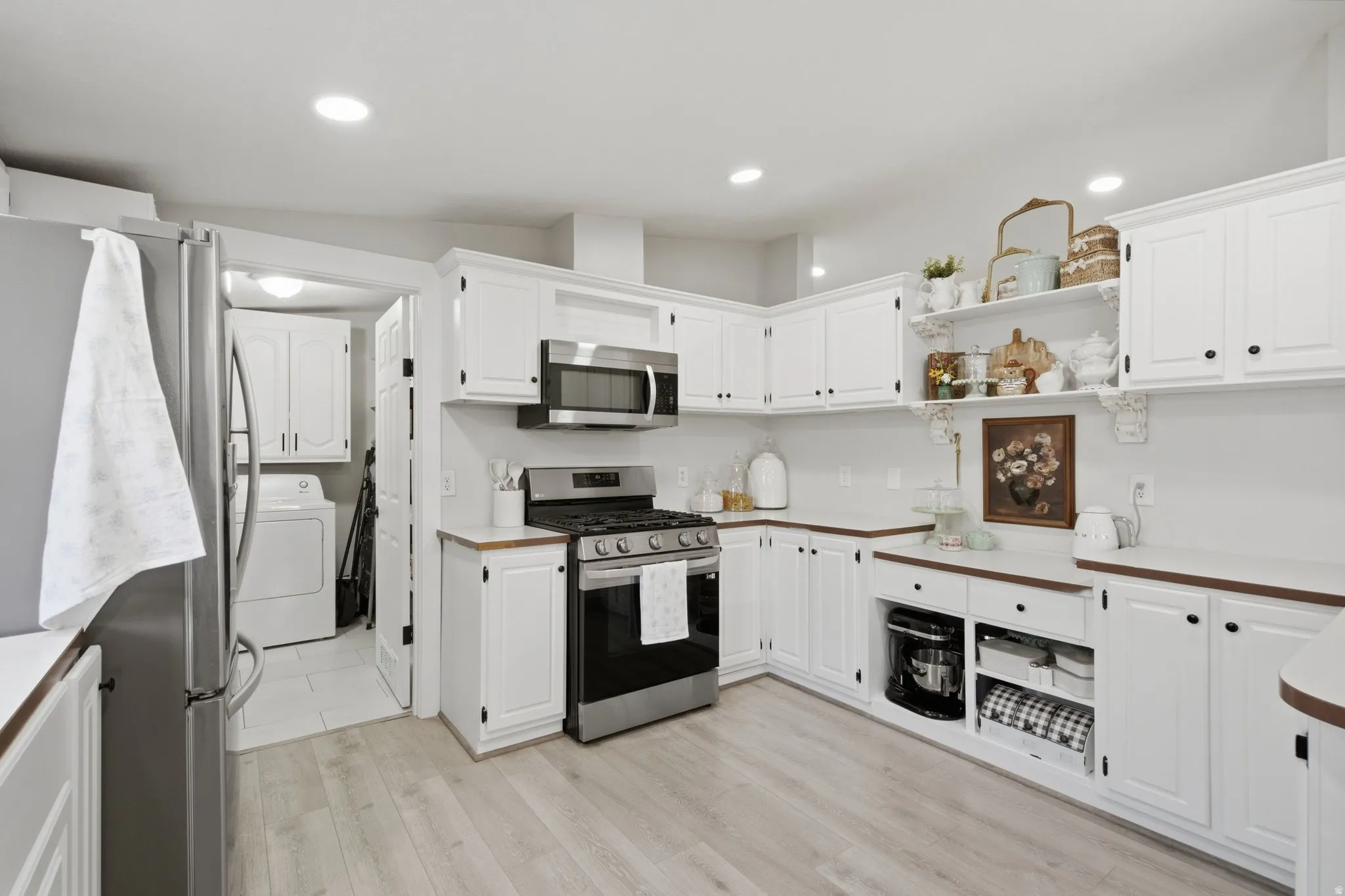 Kitchen featuring wood-finish flooring, white cabinetry with dark hardware, stainless steel appliances including a gas range and microwave, and open shelving