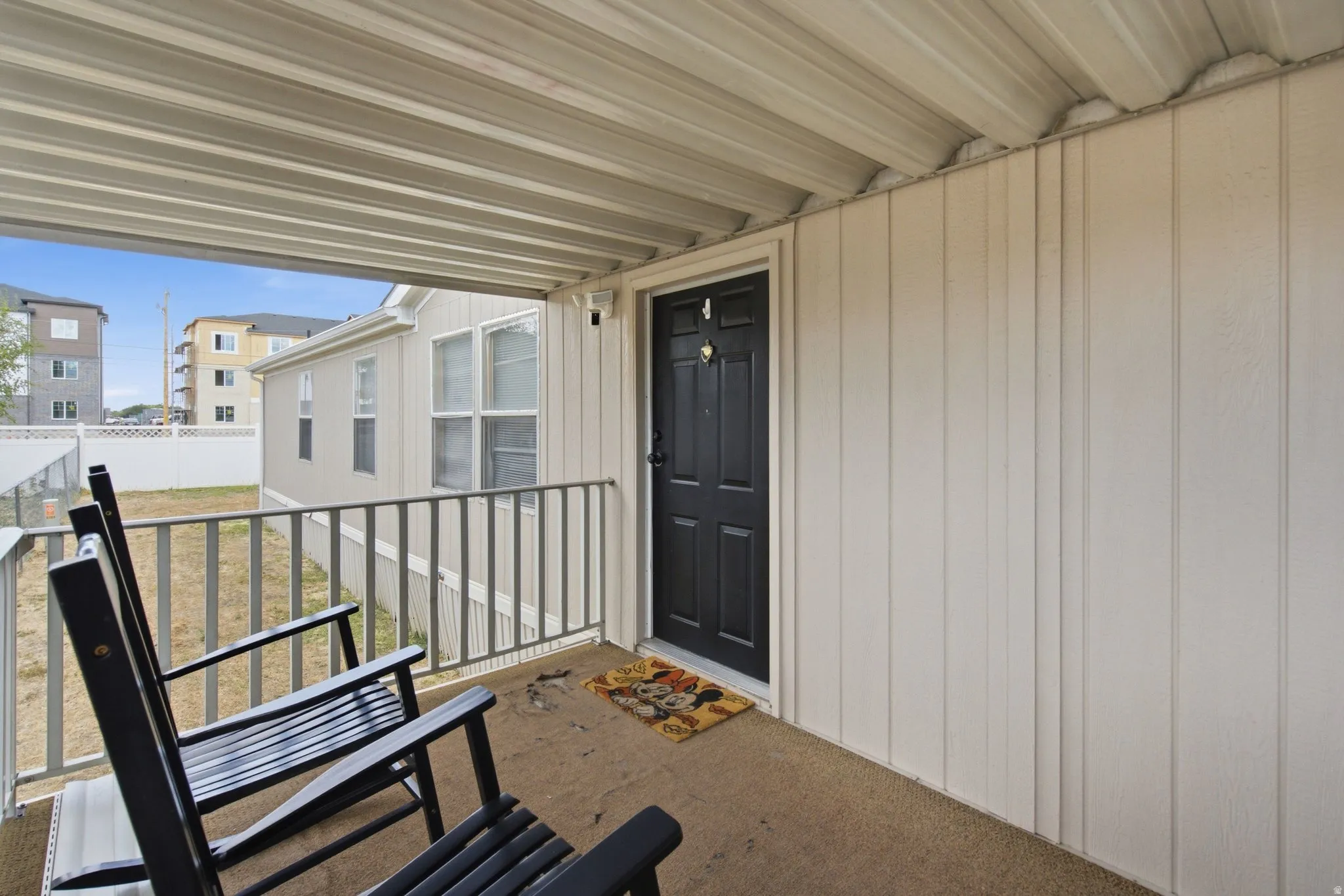 Covered front porch featuring a dark paneled entry door, vertical plank siding, and a corrugated metal ceiling