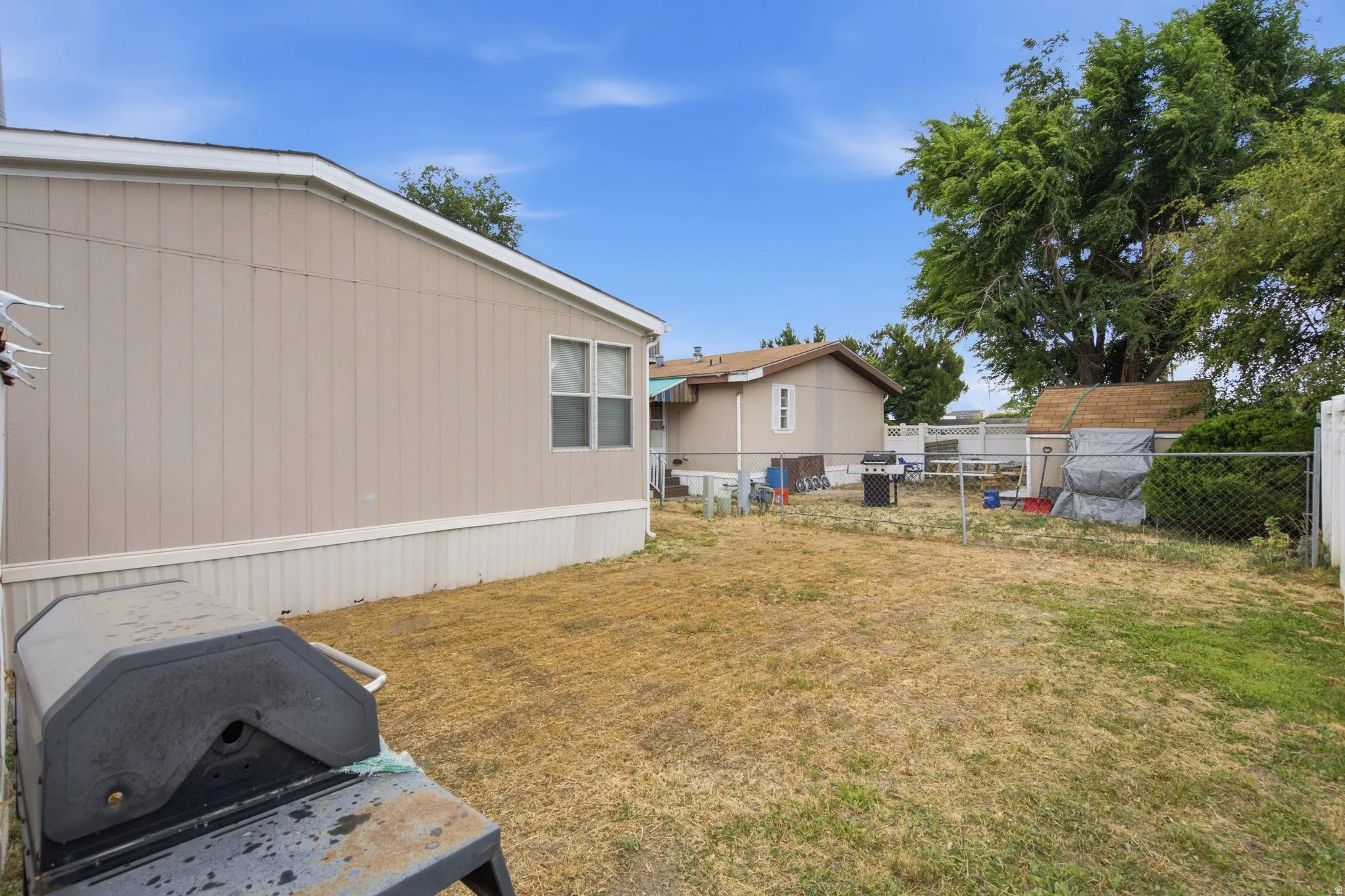 Spacious rear yard featuring a chain-link fence, mature trees, and a storage shed