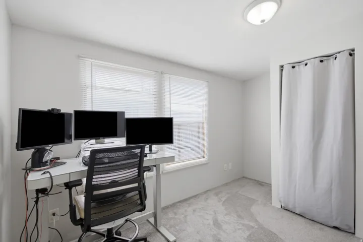 Bright room featuring two windows with horizontal blinds, neutral wall paint, and gray patterned carpeting