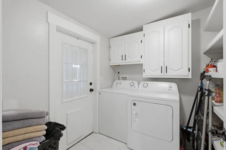 Dedicated laundry space featuring a windowed door, white cabinetry with dark hardware, built-in shelving, and tile flooring