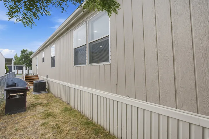 Light-toned vertical siding exterior featuring multiple windows with blinds, an air conditioning unit, and a wooden staircase leading to an entry