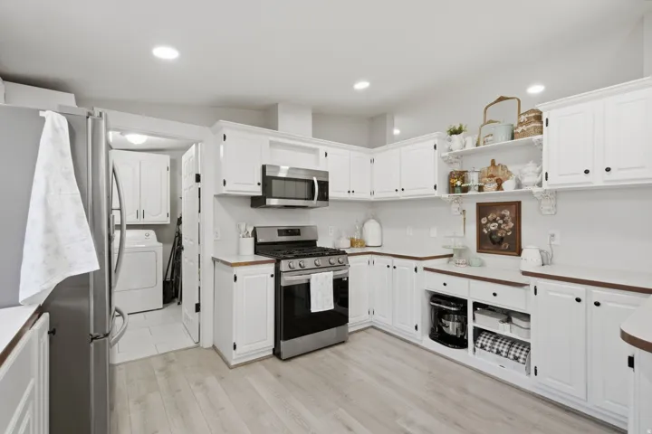 Kitchen featuring wood-finish flooring, white cabinetry with dark hardware, stainless steel appliances including a gas range and microwave, and open shelving