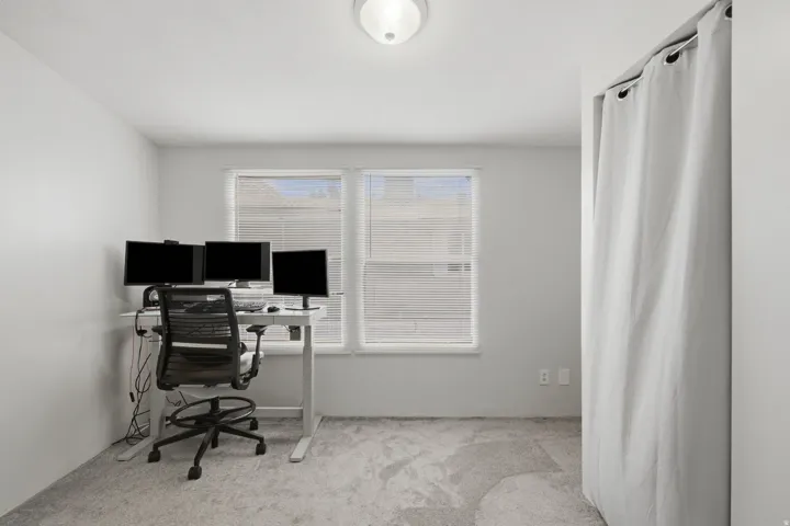 Room featuring light gray carpeting, two windows with blinds, a ceiling-mounted light fixture, and a curtained alcove