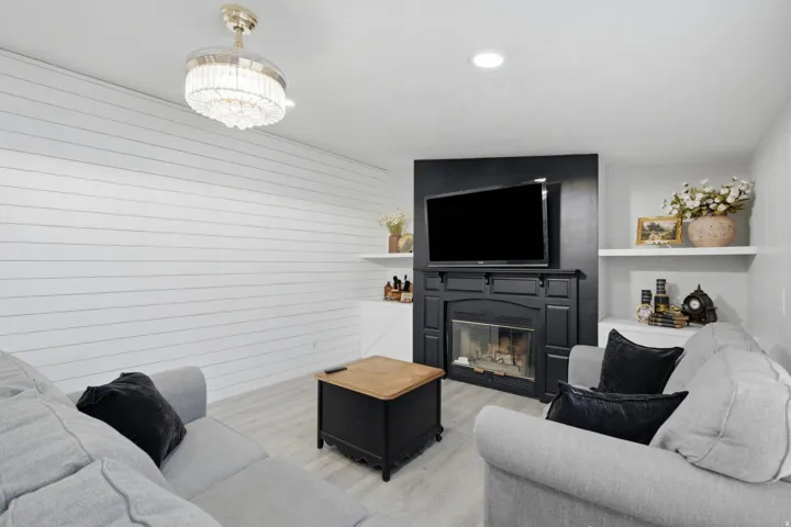 Contemporary living area featuring a prominent black fireplace with a mantel, integrated shelving units, and light wood-finish flooring
