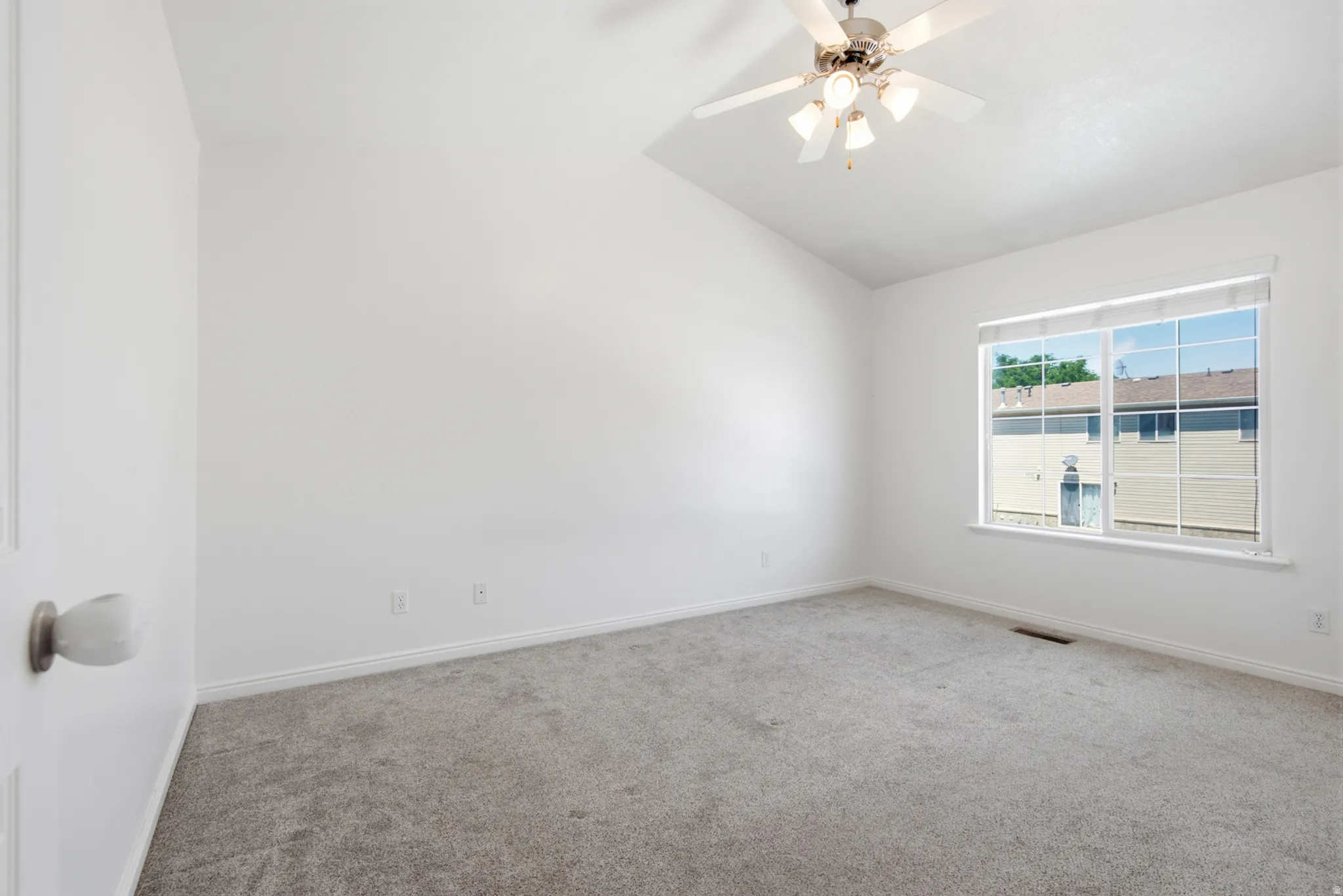 Bright room featuring vaulted ceilings, neutral gray carpeting, a large window, and a ceiling fan with integrated lighting