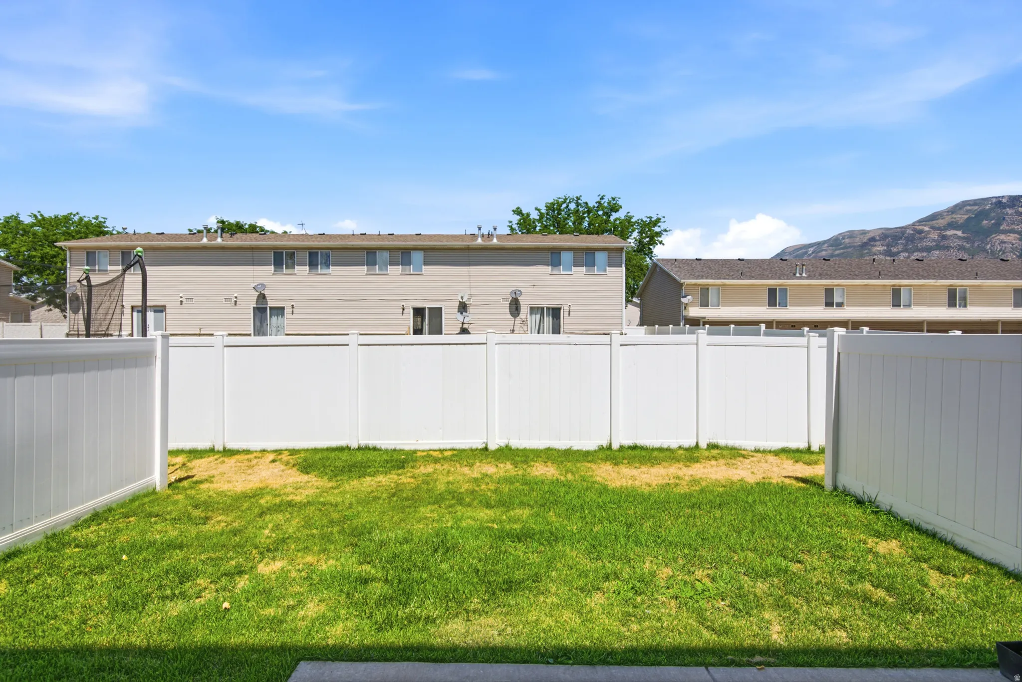 Fenced backyard with a grassy lawn, featuring white vinyl fencing and a backdrop of distant mountains