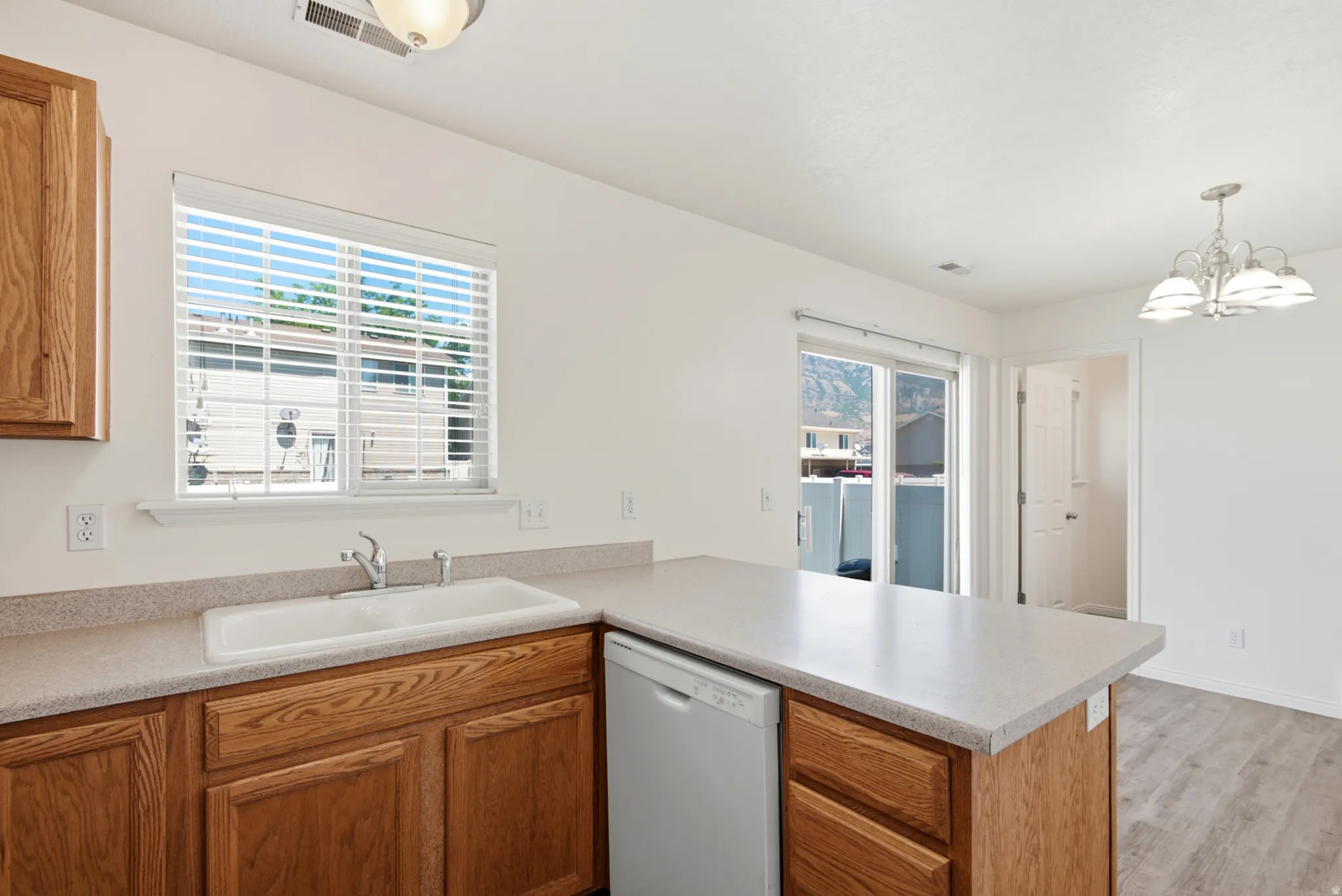 Kitchen featuring wood-finish cabinetry, solid surface countertops, a double basin sink with chrome faucet, and a built-in dishwasher