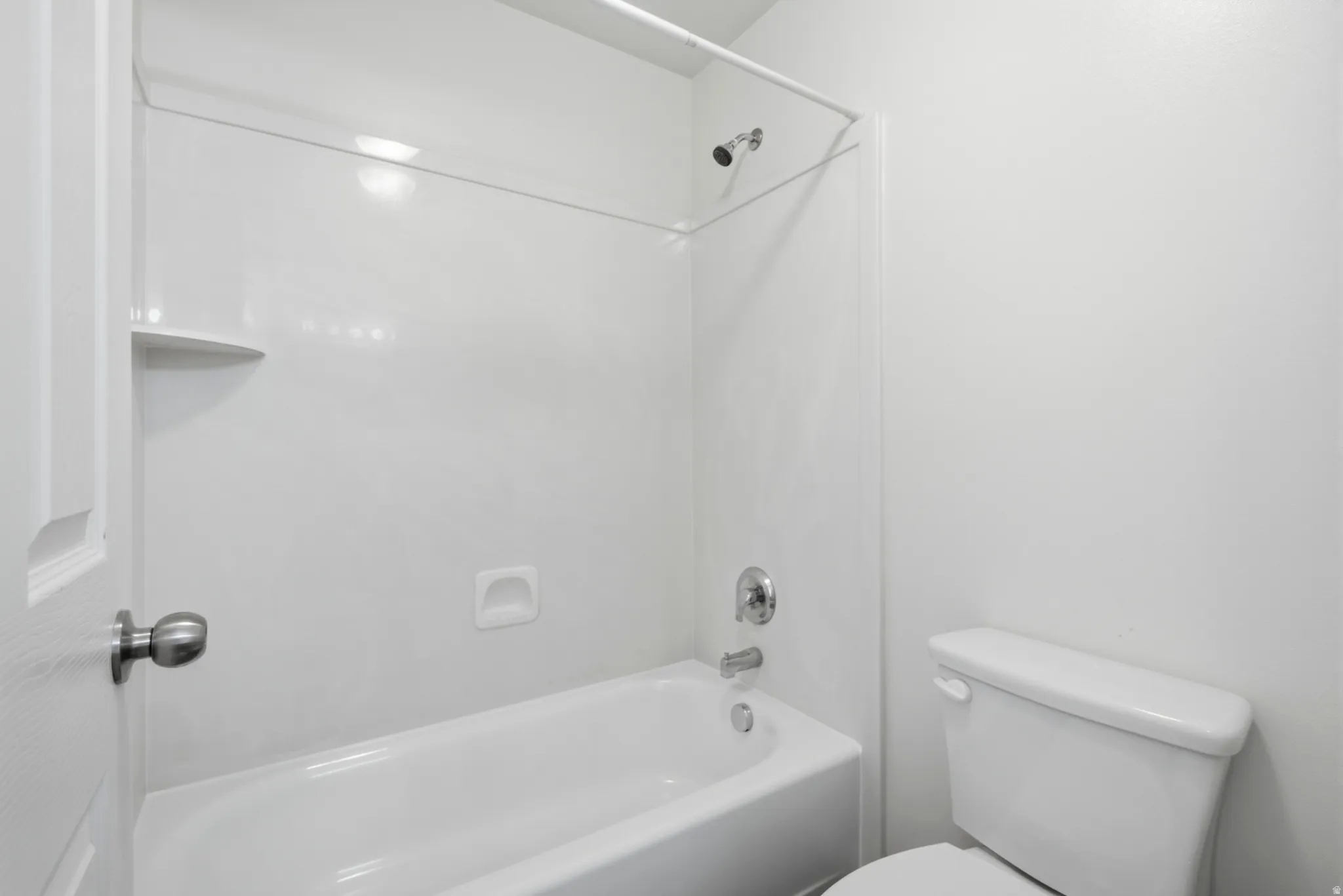 White acrylic tub and shower combination with chrome fixtures, an integrated soap dish, and a corner shelf