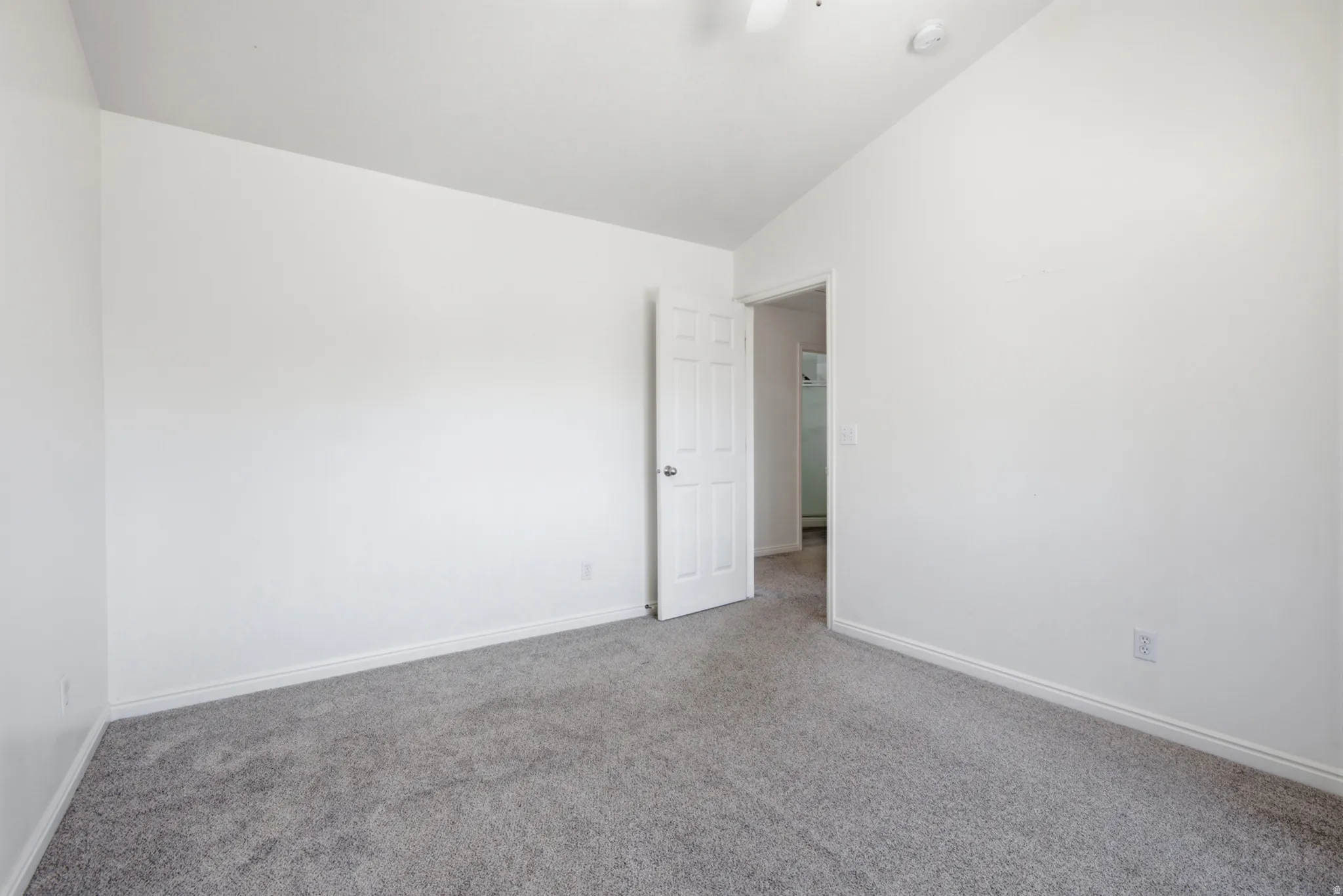 Spacious room featuring neutral paint, gray carpeting, white trim, and a ceiling fan