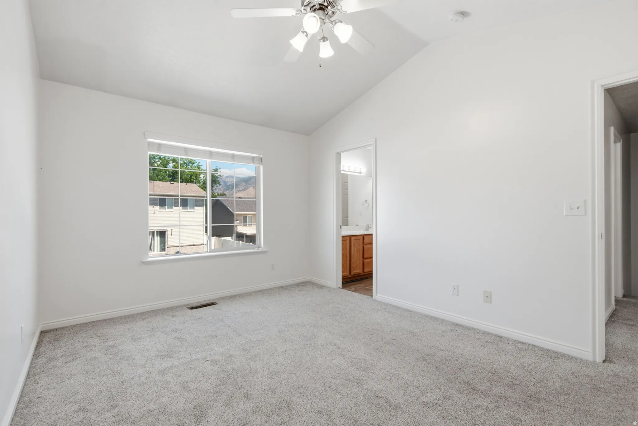 Spacious room featuring vaulted ceilings, a ceiling fan with light fixture, light gray carpeting, and white baseboards