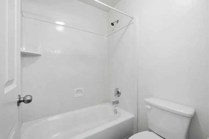 White acrylic tub and shower combination with chrome fixtures, an integrated soap dish, and a corner shelf