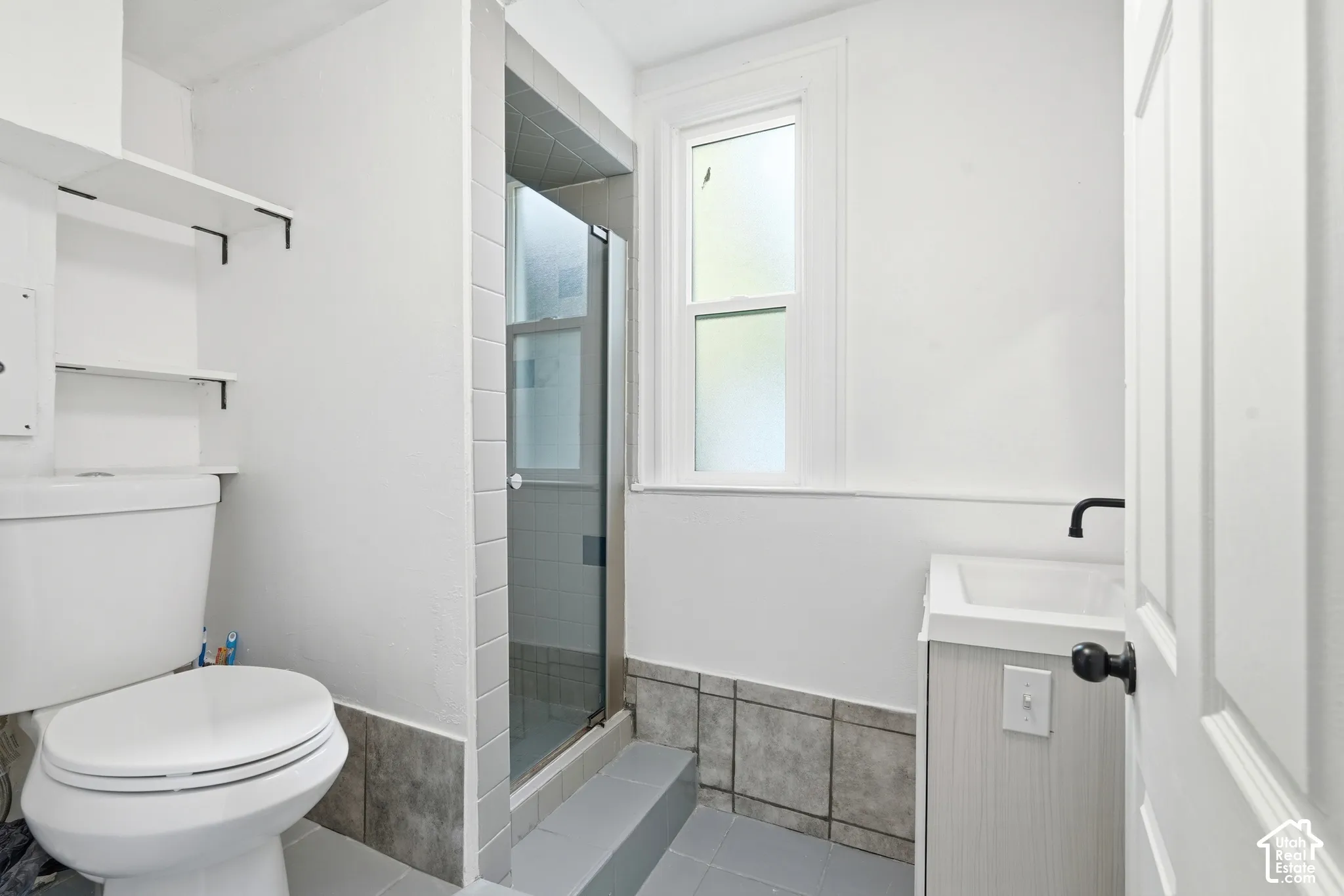 Bathroom featuring a glass-enclosed shower, a frosted window, a pedestal sink with a matte black faucet, and tiled flooring