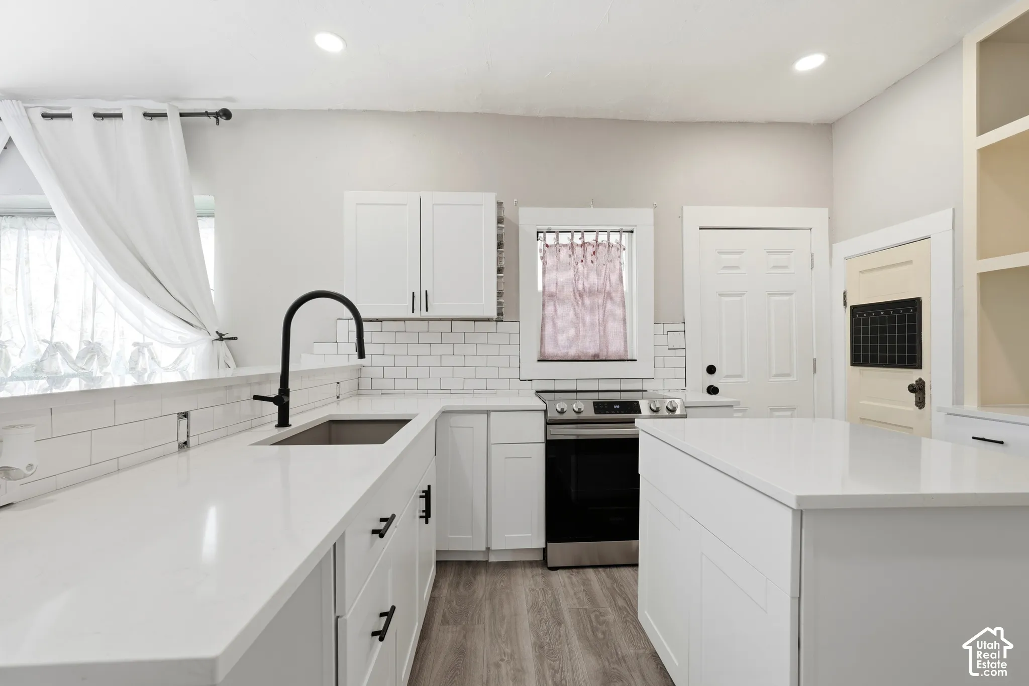 Bright kitchen featuring white shaker cabinetry, white subway tile backsplash, matte black hardware, stainless steel appliances, and wood-finish flooring