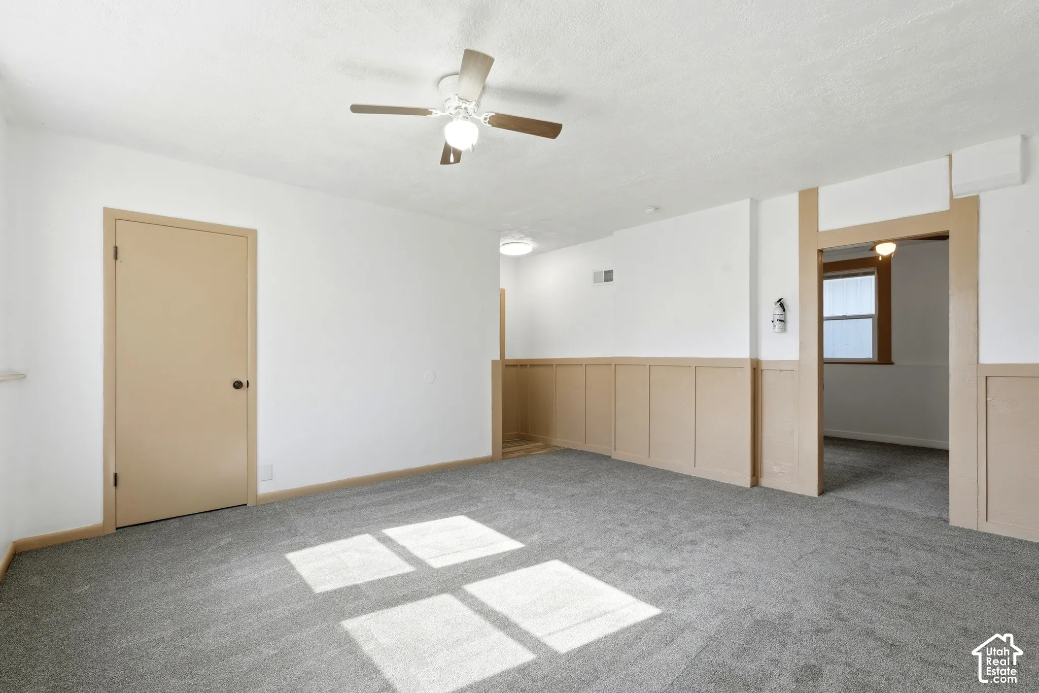 Spacious room featuring neutral carpeting, white walls with wainscoting, and a ceiling fan