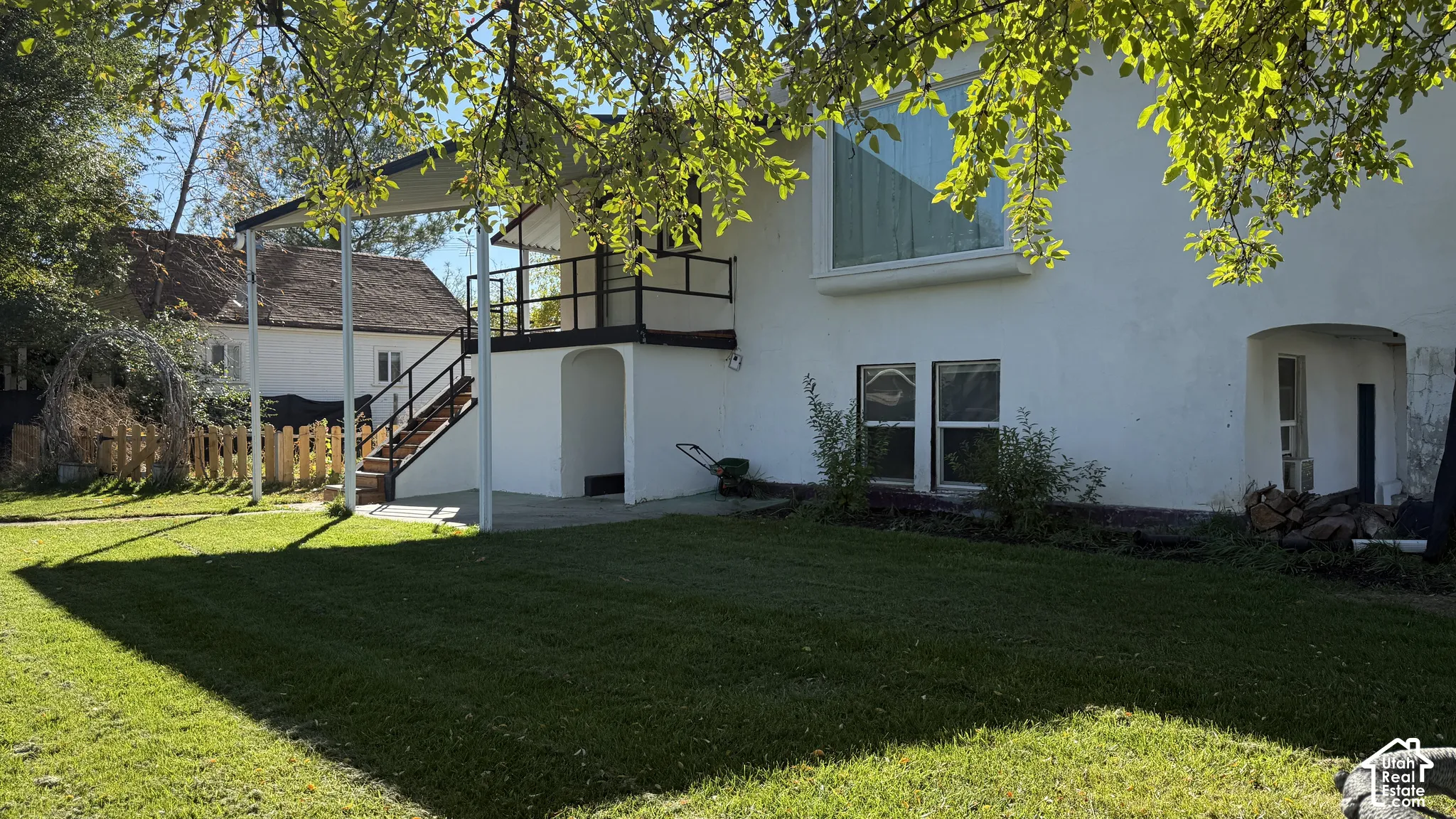 Backyard featuring a paved patio, elevated deck with railing, arched entryway, and mature tree canopy