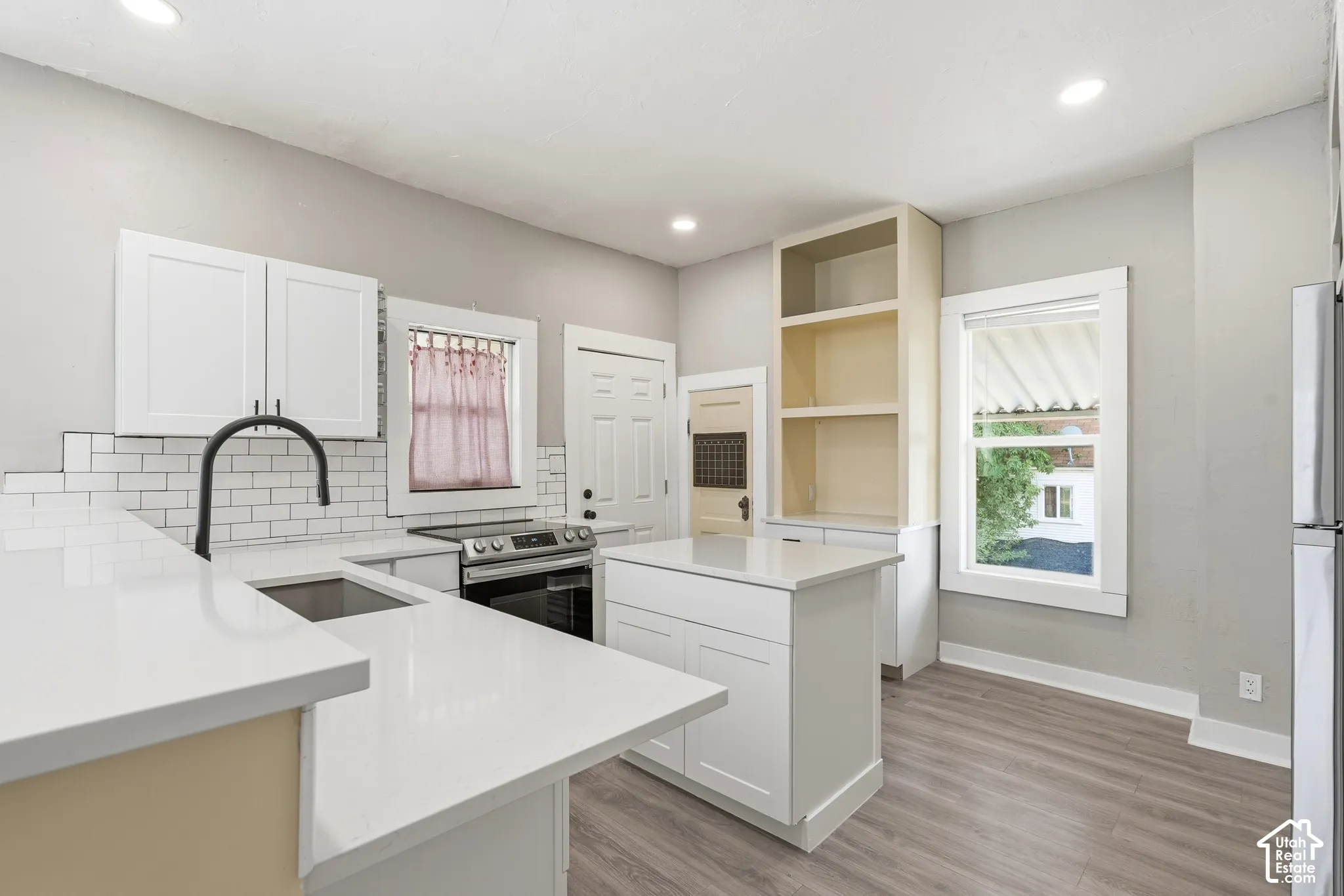 Open-concept kitchen featuring white shaker cabinetry, an island with countertop seating, stainless steel appliances, a subway tile backsplash, and light wood-finish flooring