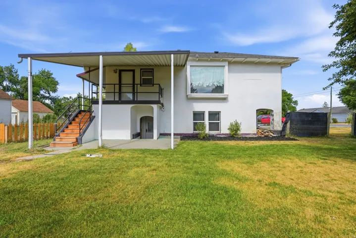 Spacious backyard featuring a covered patio, exterior staircase with black railings, and a ground-level arched entry