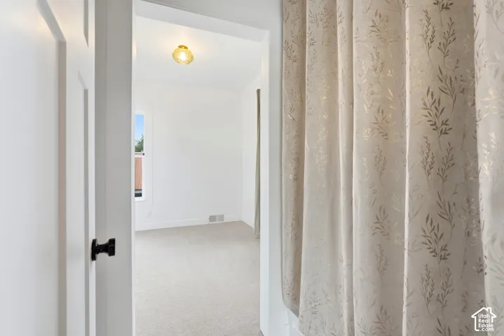 Room entry featuring a white paneled door with black hardware, leading to a space with light-toned carpet flooring, white walls, a single window, and a ceiling-mounted light fixture