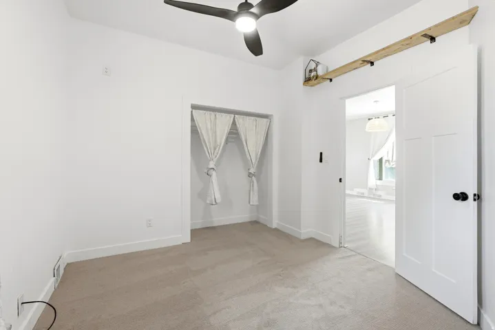 Carpeted room with a ceiling fan, a closet featuring light-colored drapes, and a white paneled door with black hardware