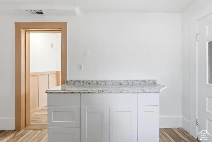 White cabinetry with a speckled countertop, light wood-finish flooring, white walls, and wood trim around an entryway