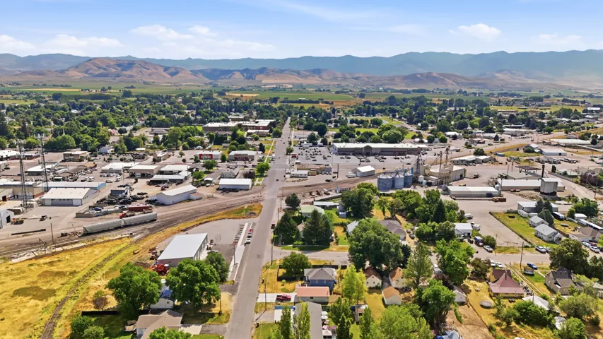 Aerial perspective showcasing a mixed-use commercial and residential district with surrounding green fields and distant mountains