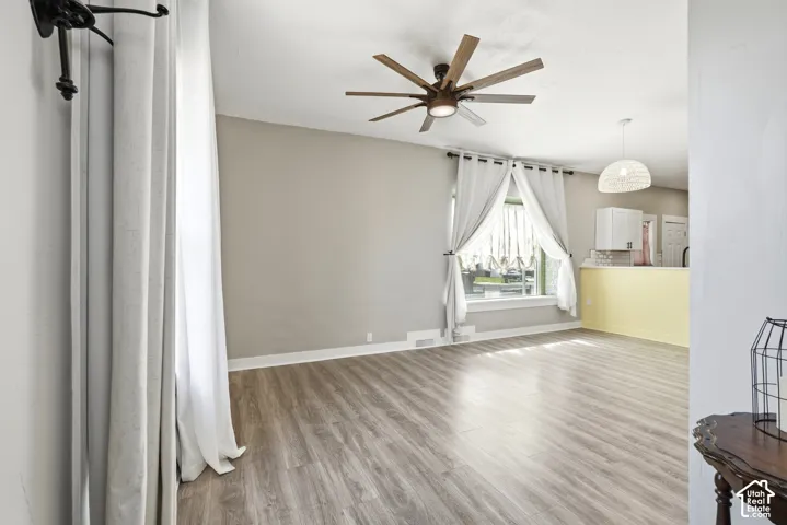 Spacious room featuring wood-finish flooring, a contemporary ceiling fan, and ample natural light from a window with white trim