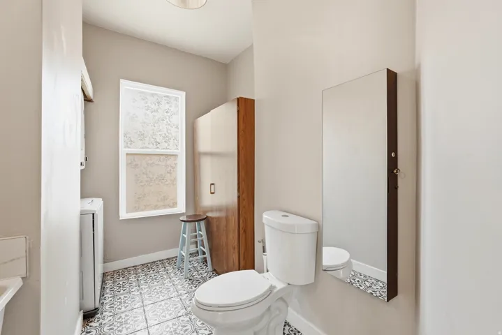 Bathroom featuring a patterned tile floor, a window with frosted glass, a white toilet, and a wall-mounted mirror