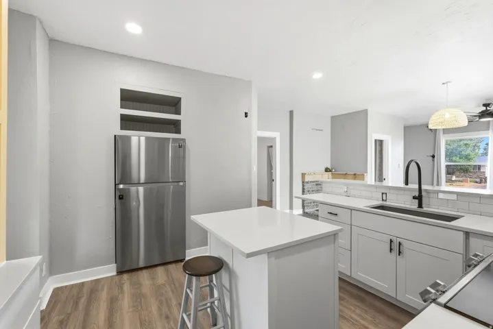 Kitchen featuring light gray cabinetry, white countertops, stainless steel refrigerator, white subway tile backsplash, and wood-finish flooring