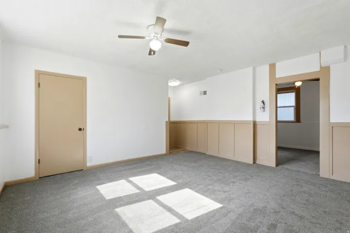 Spacious room featuring neutral carpeting, white walls with wainscoting, and a ceiling fan