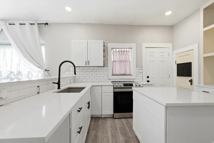 Bright kitchen featuring white shaker cabinetry, white subway tile backsplash, matte black hardware, stainless steel appliances, and wood-finish flooring