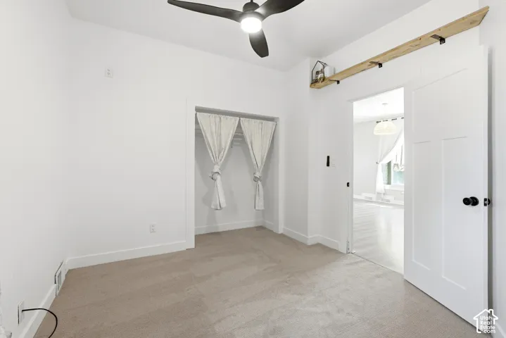 Carpeted room with a ceiling fan, a closet featuring light-colored drapes, and a white paneled door with black hardware